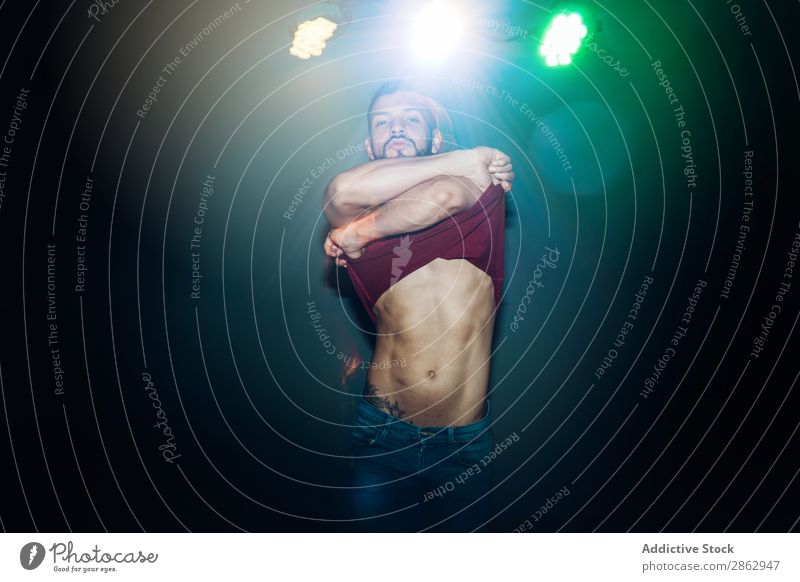 Muskulöser Mann, der sich beim Tanzen in Licht auszieht. muskulös gutaussehend sich[Akk] ausziehen Bühnenbeleuchtung zumba Bauchmuskeln Coolness Aktion Musik