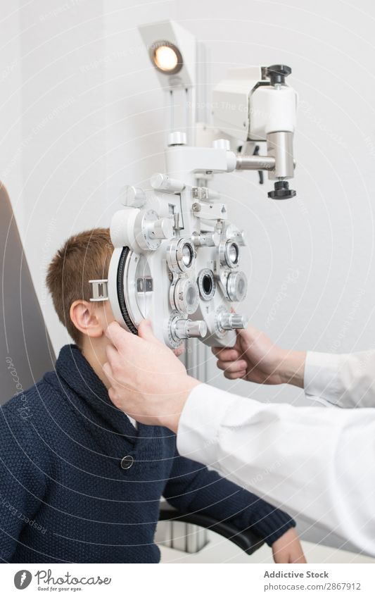 Optiker testet die Augen eines Jungen Kind Klinik Gerät diagnostizieren Anzeige Arzt Prüfung & Examen Brillenträger Gesundheit Krankenhaus Hygiene Medikament