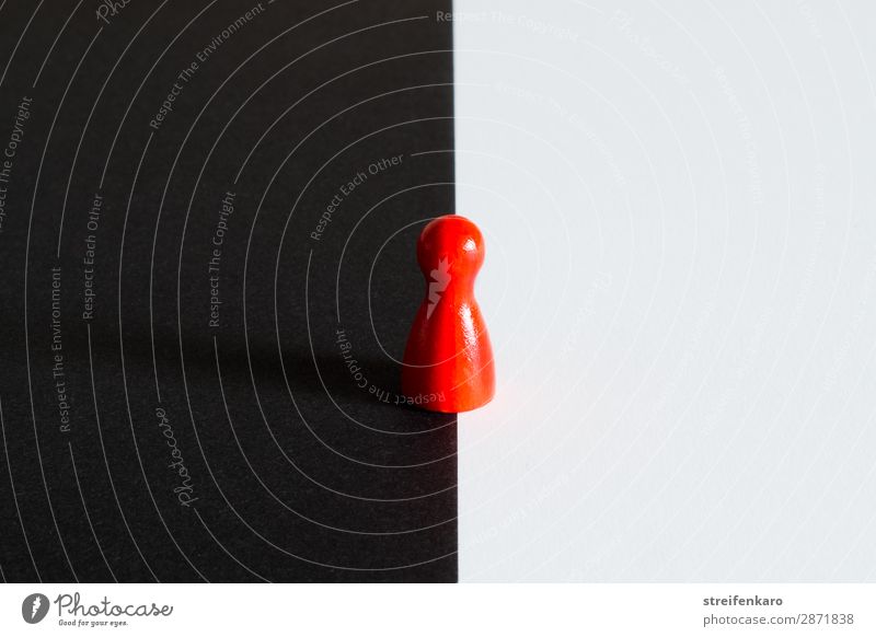 Rote Spielfigur steht auf der Grenze von schwarzem zu weißem Untergrund Spielzeug Holz dunkel Unendlichkeit Neugier rebellisch rot Mut beweglich Interesse