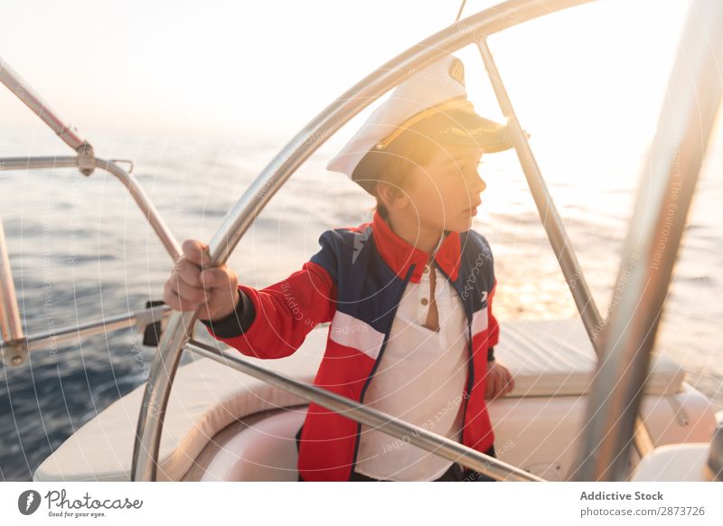 Lächelndes Mädchen hält das Lenkrad auf der Yacht auf dem Wasser. Jacht Kapitän Hut Meer Kind fliegend Schönes Wetter Wasserfahrzeug teuer aussruhen positiv