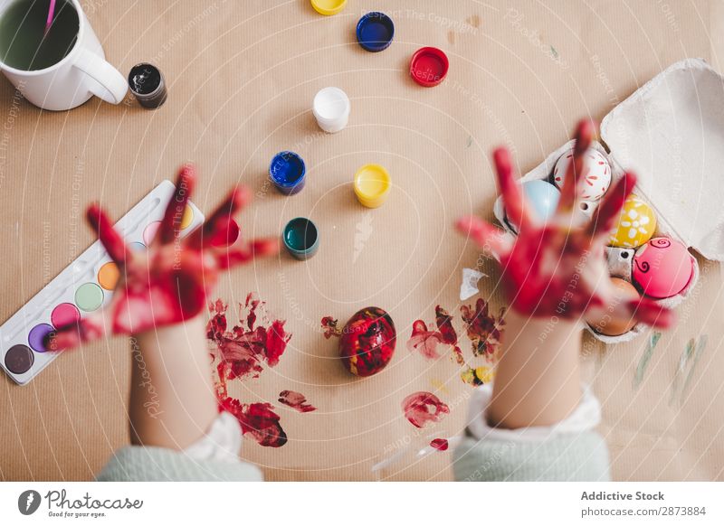 Kind zeigt schmutzige Hände in der Nähe von Hühnereiern und Farben am Tisch. Hand Ostern Ei dreckig zeigen malen Handfläche Hähnchen Container Frühling Kulisse