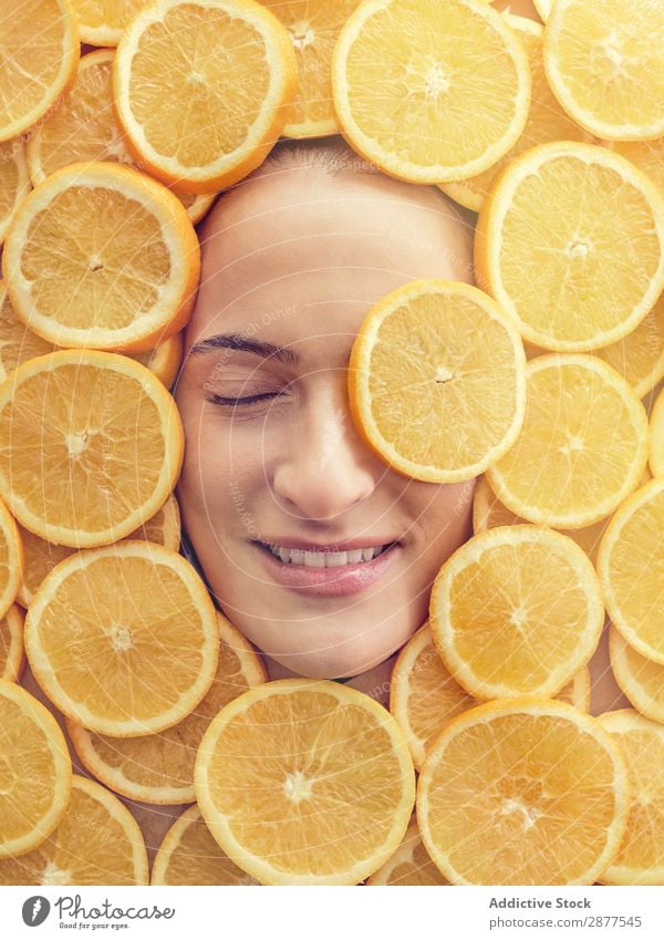 Lächelnde Frau zwischen den Orangenscheiben Gesicht Scheibe frisch Entwurf Glück Jugendliche schön Beautyfotografie Gesundheit attraktiv Frucht Fürsorge Freude