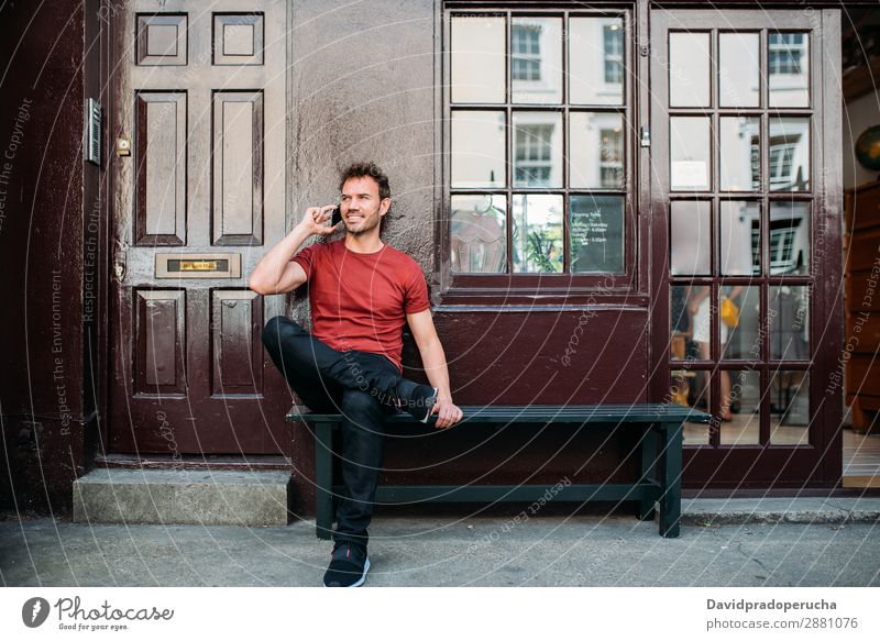 Mann sitzt auf einer Bank auf einem schönen kastanienbraunen Hintergrund. Handy Kaukasier heiter Gebäude Jugendliche Architektur Technik & Technologie