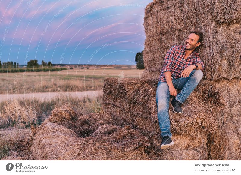 Ein glücklicher Mann sitzt auf einem Haufen Heu. Landwirt Sommer Kaukasier Landschaft Natur Länder Himmel Erholung Lifestyle Arbeit & Erwerbstätigkeit
