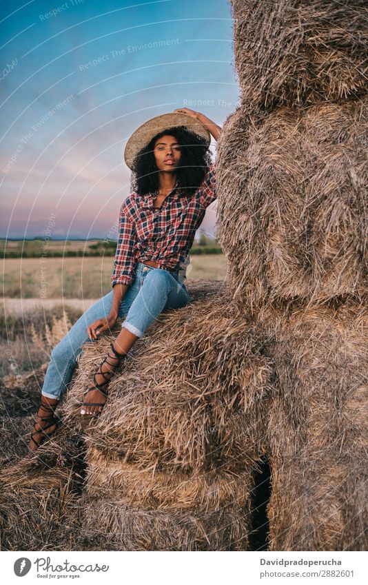 Glückliche schwarze junge Frau, die auf einem Haufen Heu sitzt. Landwirt Sommer urwüchsig Afrikanisch Landschaft Natur Länder Himmel Erholung Lifestyle