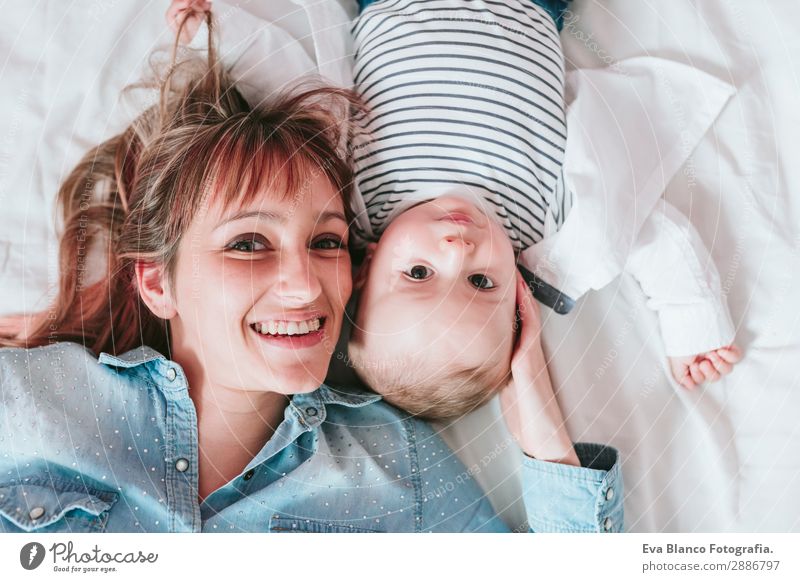 glückliche junge Mutter und ihr kleiner Junge liegen auf dem Bett und lächeln. Lifestyle Freude Glück Haut Lampe Schlafzimmer Kind Mensch maskulin feminin Baby