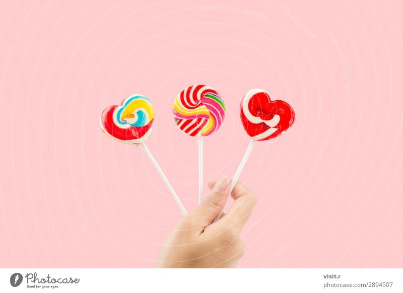 Frauenhand hält drei farbenfrohe Lollis. Lebensmittel Dessert Süßwaren Stil Freude Erwachsene Hand Herz Liebe hell lecker retro rosa rot weiß Farbe Geschenk