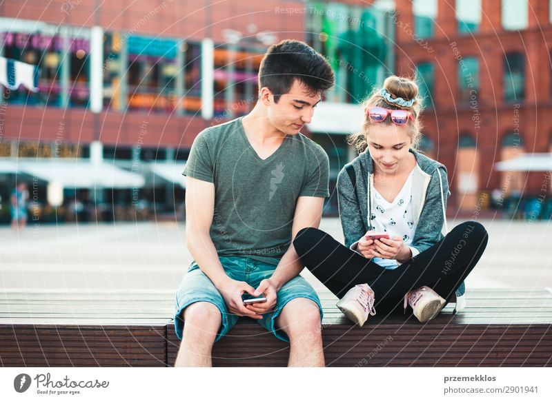 Ein befreundetes Paar, ein Mädchen und ein Junge im Teenageralter, die sich gemeinsam mit Smartphones amüsieren, im Stadtzentrum sitzen und Zeit miteinander verbringen