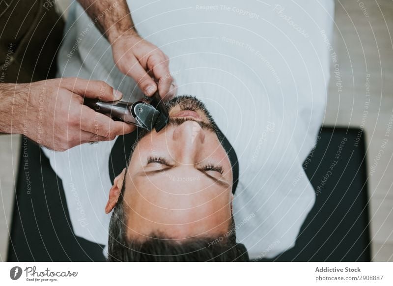 Barbier schneidet Bart zu Mann im Salon Friseursalon Schneiden Vollbart Hand Trimmer Kamm Stil professionell sitzen Mode Lifestyle Erwachsene Reichtum Kunde