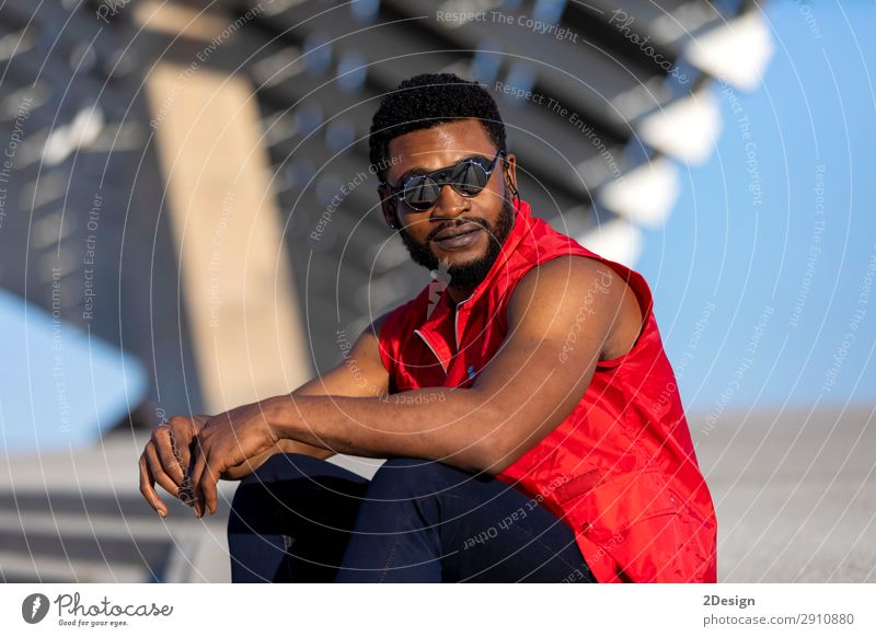 Junger schwarzer Mann mit Sonnenbrille, der auf der Treppe sitzt. elegant Stil Erholung Erwachsene Bekleidung Jeanshose Afro-Look sitzen Coolness trendy jung