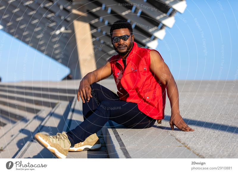 Junger schwarzer Mann mit Sonnenbrille, der auf der Treppe sitzt. elegant Stil Erholung Erwachsene Bekleidung Jeanshose Afro-Look sitzen Coolness trendy jung