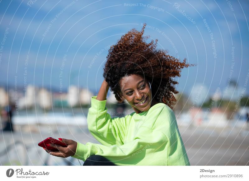 Seitenansicht einer jungen lockigen Afrofrau, die auf dem Wellenbrecher sitzt. Lifestyle Stil schön Haare & Frisuren Meer Musik Telefon PDA Mensch feminin