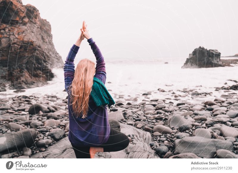 Frau auf Steinen in der Nähe der Meeresküste meditierend hochgezogene Hände Felsen Wasser Hügel Geschwindigkeit platschen Energie Jugendliche Natur Yoga