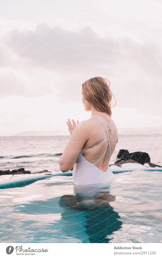 Frau sitzt im Pool in der Nähe von Steinen. Schwimmbad Jugendliche aussruhen Wasser geschlossene Augen Felsen Himmel Wolken Sommer Körper Erholung Gesundheit