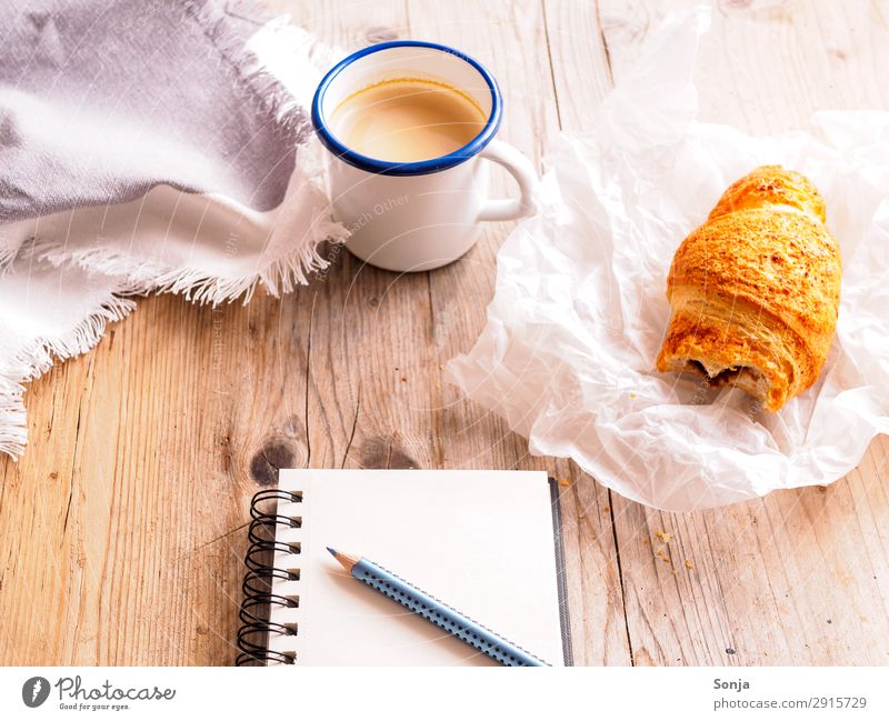 Kaffepause mit Croissant Lebensmittel Teigwaren Backwaren Ernährung Frühstück Kaffeetrinken Getränk Heißgetränk Becher Schreibwaren Papier Zettel Schreibstift