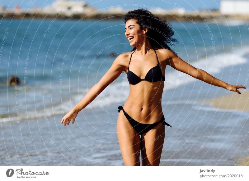 Junge arabische Frau in Badebekleidung, die an einem tropischen Strand lächelt. Lifestyle Glück schön Körper Haare & Frisuren Haut Freizeit & Hobby