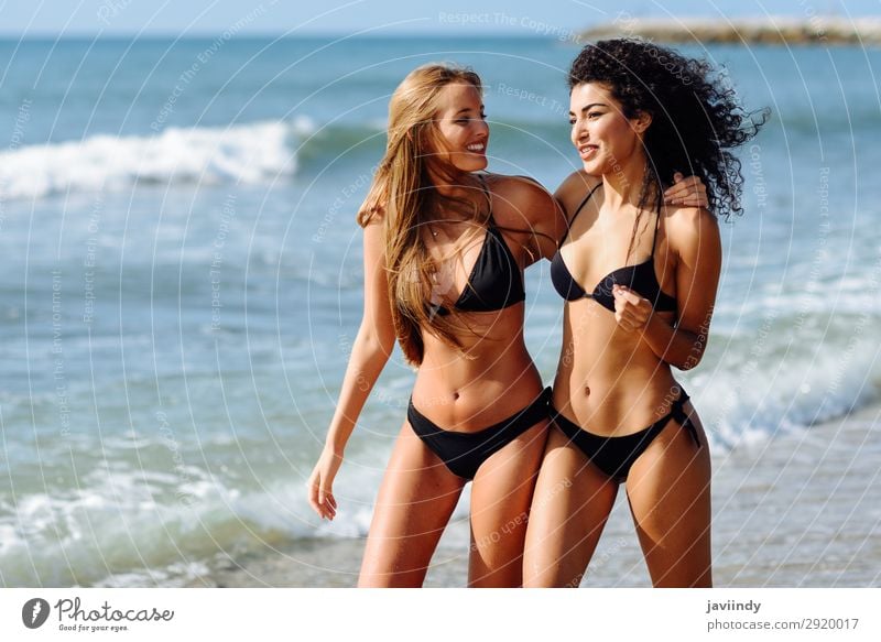 Zwei junge Frauen mit schönen Körpern in Bademode an einem tropischen Strand, die einen Spaziergang am Ufer machen. Lifestyle Freude Glück Haare & Frisuren