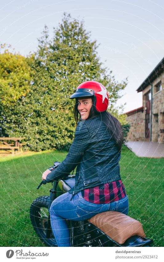 Frau mit Helm auf einem Custom-Motorrad Lifestyle Glück schön Haus Mensch Erwachsene Baum Gras Verkehr Fahrzeug Mode Jeanshose Lächeln authentisch retro
