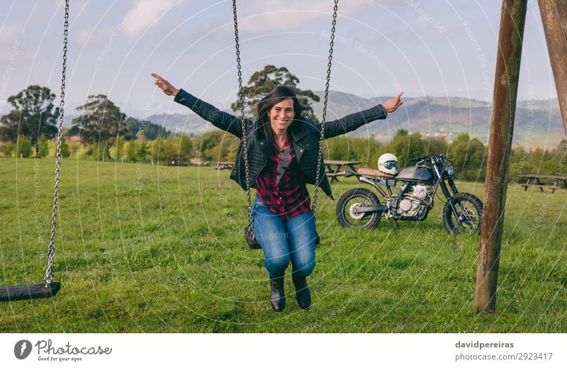 Junge Frau schaukelt im Erholungsgebiet mit Motorrad im Hintergrund Lifestyle Glück schön Freiheit Mensch Erwachsene Natur Baum Gras Park Wiese Fahrzeug Mode