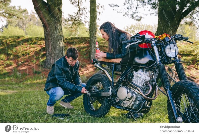 Mann repariert sein Motorrad, während seine Freundin ihn ansieht. trinken Erfrischungsgetränk Alkohol Bier Lifestyle Ferien & Urlaub & Reisen Ausflug sprechen