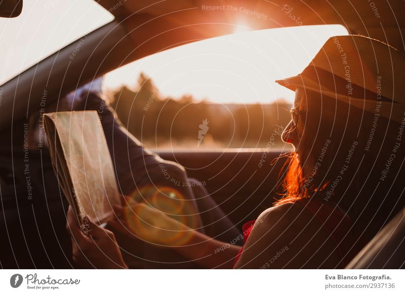 Modernes Mädchen, das in einem Auto ruht und bei Sonnenuntergang eine Karte liest. Lifestyle Freude Erholung Freizeit & Hobby lesen Ferien & Urlaub & Reisen