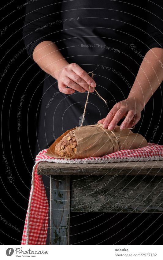 Mädchen in schwarzer Kleidung wickelt einen ganzen gebackenen Laib Brot ein. Brötchen Ernährung Essen Frühstück Tisch Küche Seil Frau Erwachsene Hand 1 Mensch