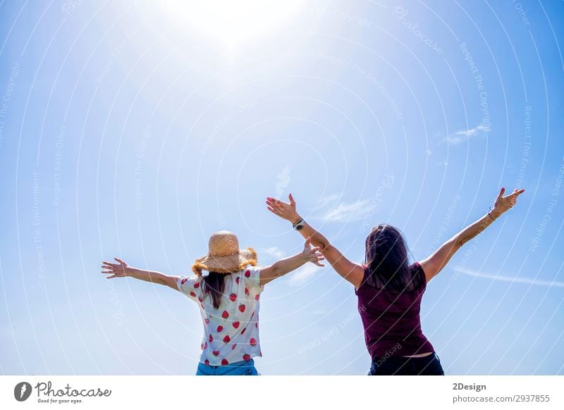 Zwei junge Frauen sitzen auf einem Zaun, die Arme sind gegen den blauen Himmel erhoben. Lifestyle Freude Glück schön Erholung Freizeit & Hobby