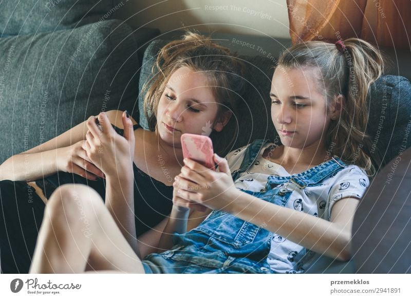 Junge Frauen, die Mobiltelefone benutzen, Musikclips anschauen, SMS und Nachrichten schreiben. Teenager, die die Smartphones benutzen und zu Hause auf dem Sofa sitzen. Benutzen technische Geräte. Mädchen tragen Sommerkleidung