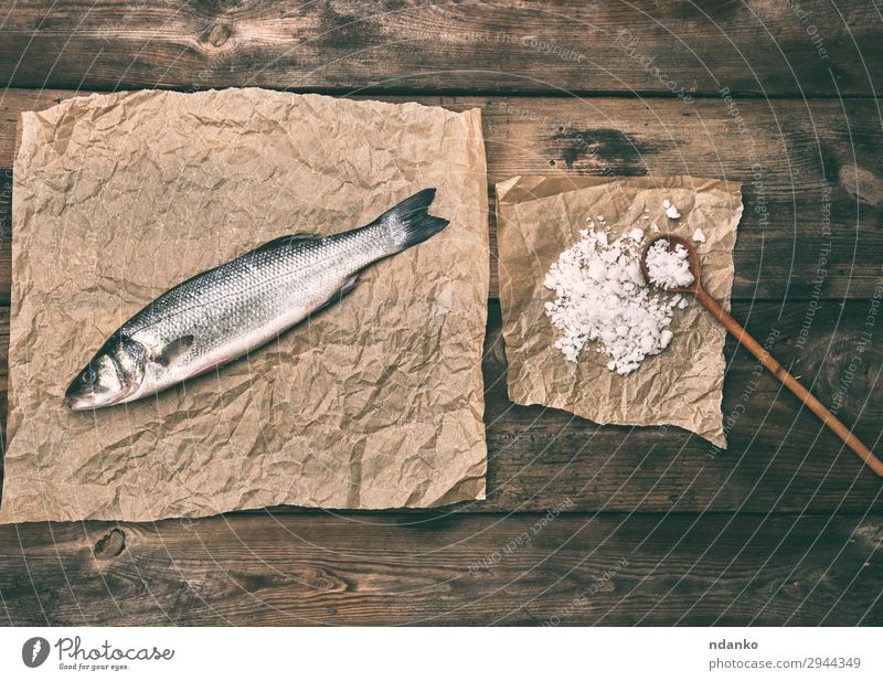 Seebarschfisch auf braunem Knitterpapier Fisch Meeresfrüchte Ernährung Löffel Küche Tier Papier Holz frisch oben grau Salz Bass Holzplatte Essen zubereiten