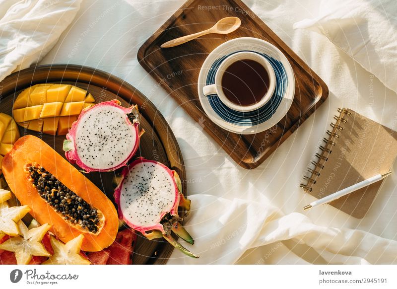 Kaffee oder Tee auf Holztablett und tropischem Obstteller exotisch Karambole Mango Pitahaya Drachenfrucht Teller Gesunde Ernährung Pflanzenbasiert