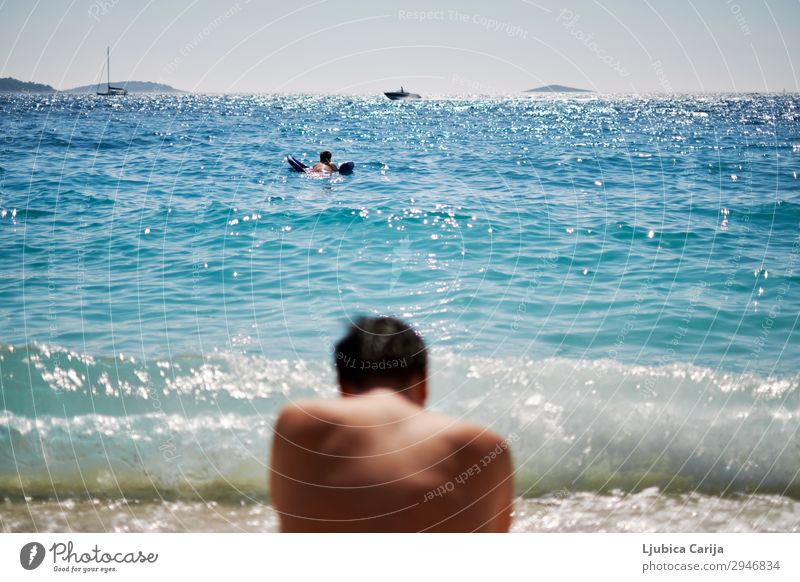 Junger Mann sitzt an einem Strand und schaut auf die Wellen. Erholung Sommer Schwimmen & Baden Segeln Mensch maskulin Jugendliche Rücken 2 Wasser Himmel
