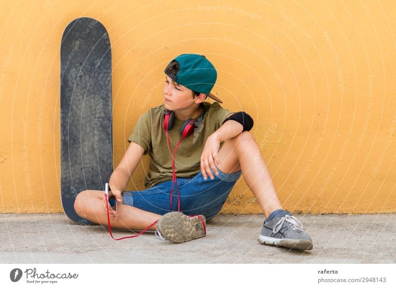 Junge, der auf dem Boden sitzt und sich an eine Wand lehnt, während er ein Handy benutzt. Kind Telefon PDA Technik & Technologie Mensch maskulin Jugendliche 1