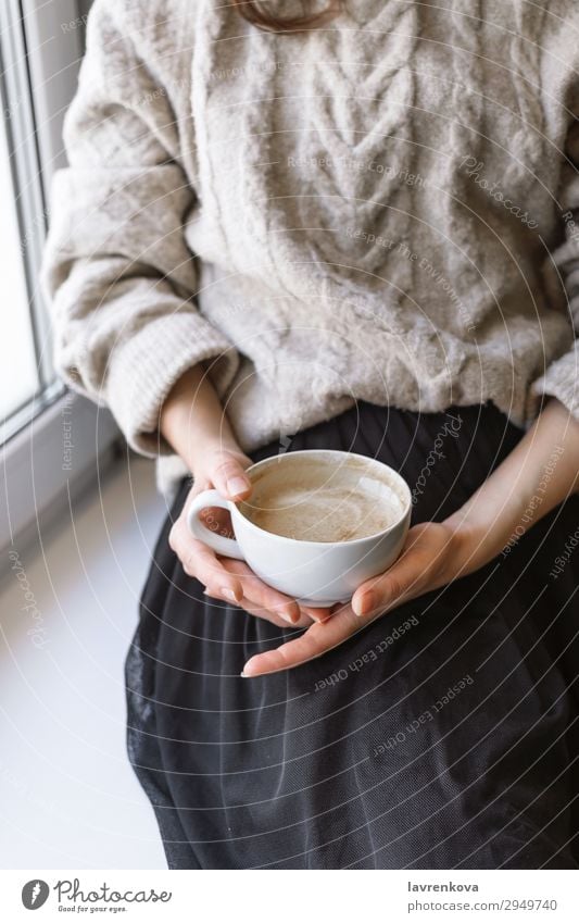 Damenhaltebecher mit Latte vor dem Fenster Herbst Winter Erholung Pullover Frühstück Innenaufnahme Hand Tasse Becher Wärme gemütlich Café Nahaufnahme Kaffee