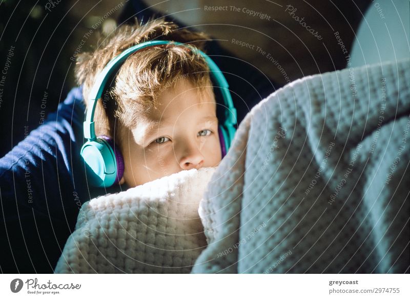 Eine Nahaufnahme eines Jungen mit Kopfhörern, zugedeckt mit einer Decke Erholung Musik Headset hören Blick Hörmuscheln ruhen Freizeit Sonnenschein Kopfkissen
