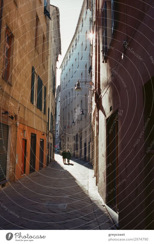 Eine schmale Straße zwischen alten italienischen Gebäuden, mit einem dünnen Sonnenlicht Korridor und zwei menschliche Figuren weit weg Mensch Stadt Fußgänger