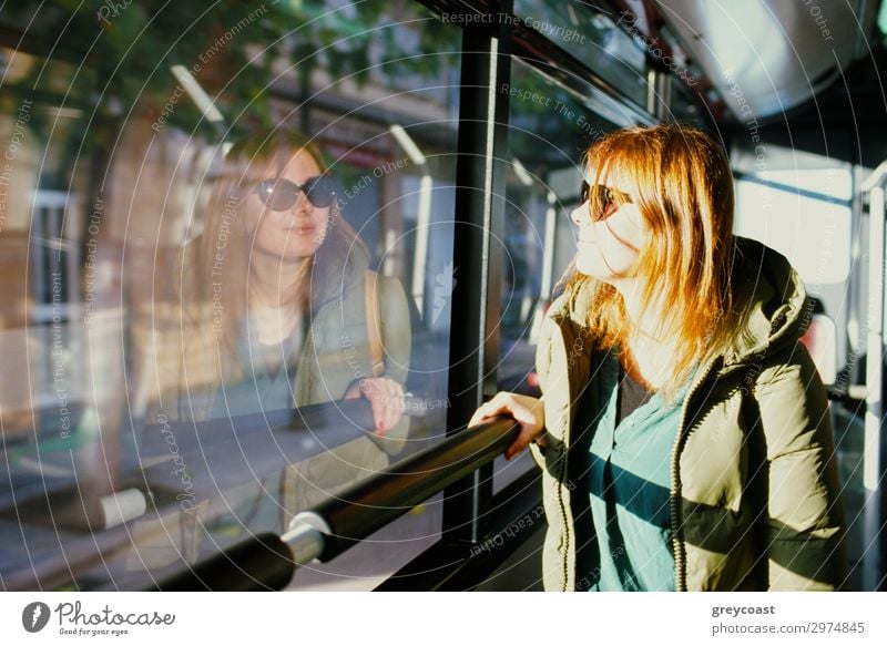 Eine junge rothaarige Frau mit Sonnenbrille betrachtet ihr Spiegelbild in einem Busfenster Ferien & Urlaub & Reisen Ausflug Städtereise Mensch Junge Frau