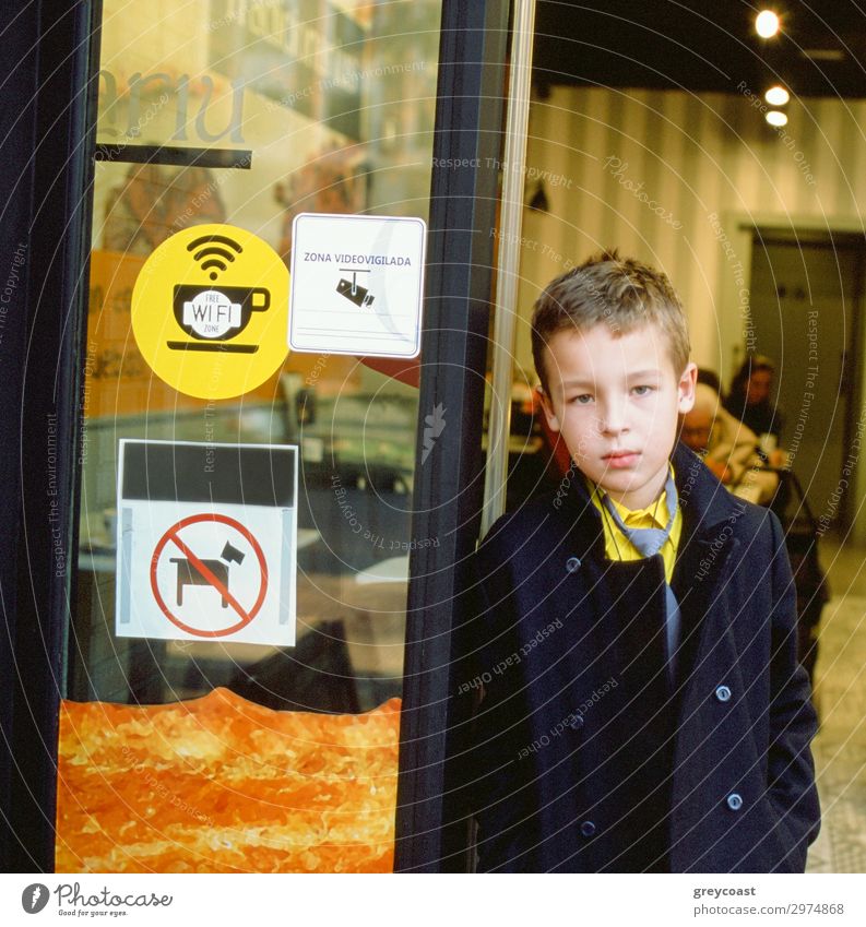 Ernster Schuljunge am Eingang des Cafés. Tür mit Aufklebern für kostenloses W-LAN, Videokameraüberwachung und Tiere verboten. Spanien Kind Schulkind Schüler