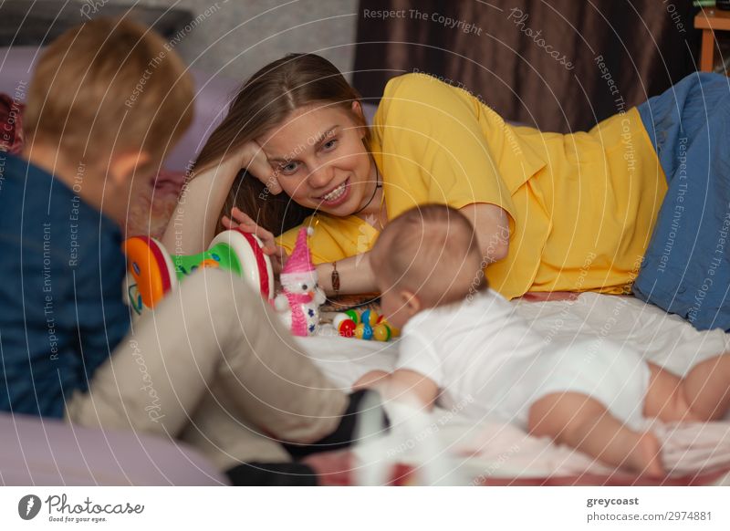 Ein neugeborenes Baby liegt auf dem Boden, umgeben von seinen Spielsachen und seiner Familie - einer Mutter und einem älteren Bruder Freude Spielen Mensch