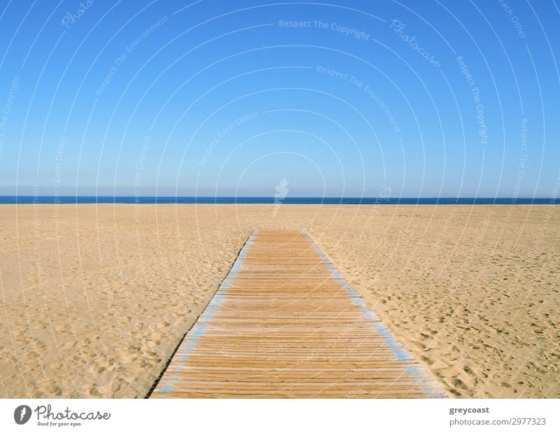 Ein gelb-blaues Bild, bei dem die blaue Hälfte der Himmel und die gelbe Hälfte der Sand und ein Holzweg darauf ist. Eine dünne dunkelblaue Linie des Meeres in der Mitte