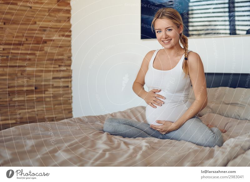 Glückliche schwangere Frau, die auf einem Bett sitzt. Kind feminin Baby Erwachsene Mutter Familie & Verwandtschaft 1 Mensch 18-30 Jahre Jugendliche blond