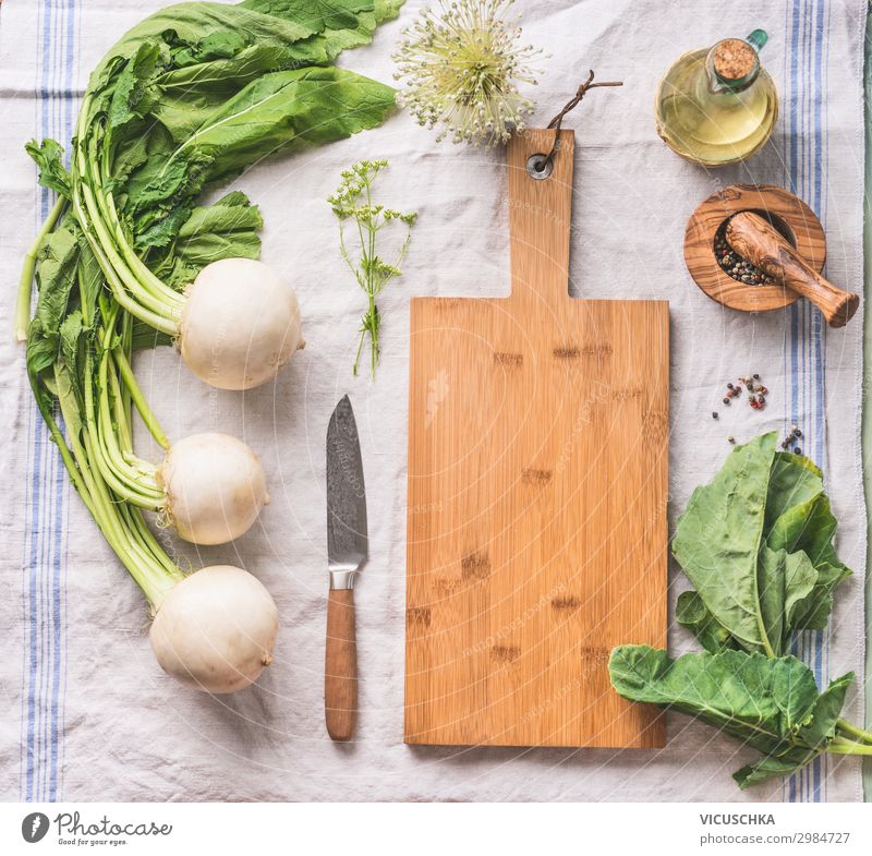 Food background with raw white radish with greens on light kitchen table with cutting board and knife, top view
