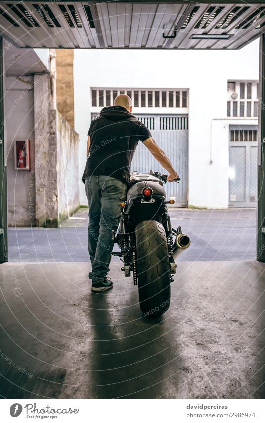 Mann mit Custom-Motorrad, der die Garage verlässt. Lifestyle Stil Ferien & Urlaub & Reisen Ausflug Mensch Erwachsene Straße Jeanshose Glatze stehen tragen
