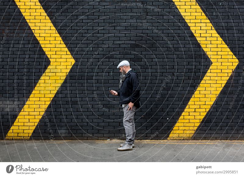 Mann vor einer schwarzen Wand mit gelben Pfeilen Mensch maskulin Erwachsene 1 Mauer Fassade Zeichen Schilder & Markierungen Hinweisschild Warnschild trendy