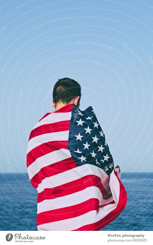 Mann von hinten in amerikanische Flagge gehüllt gegen blauen Himmel. Glück Freiheit Meer Feste & Feiern Erwachsene Hand Denkmal Streifen Fahne Ehre
