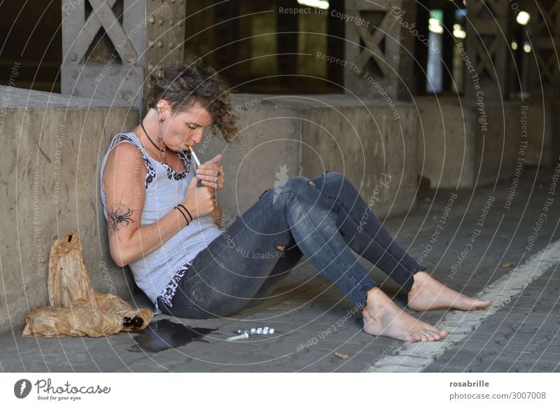 Drogenabhängige Punkerin sitzt auf der Strasse und zündet sich eine Zigarette an Alkohol Rauchen Rauschmittel Arbeitslosigkeit Frau Erwachsene 45-60 Jahre