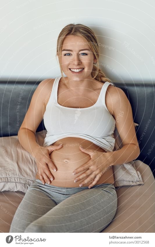 Glücklich lächelnd attraktive junge schwangere Frau Erwachsene 1 Mensch 18-30 Jahre Jugendliche Lächeln Liebe sitzen Schwangerschaft wiegend Bauch Bonden Bett
