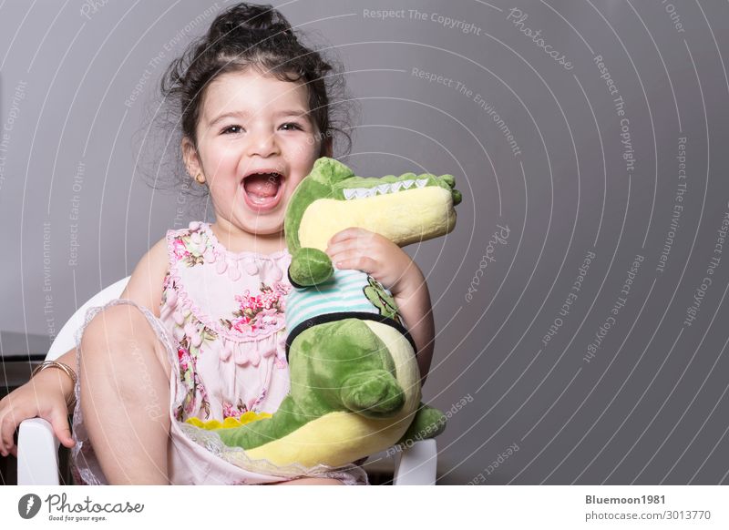 Überraschtes und fröhliches kleines Mädchen hält eine Alligatorpuppe. Lifestyle Freude Glück schön Spielen Stuhl Entertainment Kind Hand 1 Mensch 1-3 Jahre
