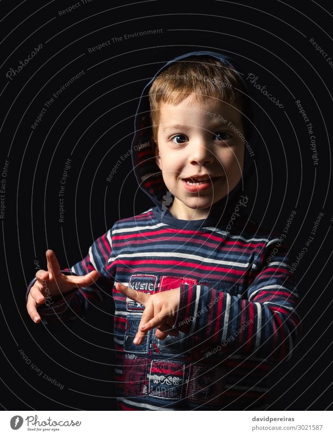 Glücklicher Junge mit Kapuzenpulli schaut in die Kamera auf schwarzem Hintergrund Freude Gesicht Kind Schulkind Mensch Mann Erwachsene Kindheit Hand Finger