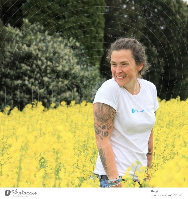 lachende brünette Frau mit weißem Shirt und Tatoos auf den Armen steht in blühendem gelbem Raps Mensch feminin Erwachsene 1 30-45 Jahre Umwelt Natur Landschaft
