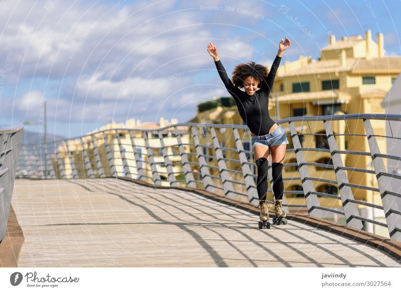 Schwarze Frau, Afrofrisur, auf Rollschuhen, die mit offenen Armen auf der Stadtbrücke im Freien fährt. Lifestyle Freude Glück schön Haare & Frisuren